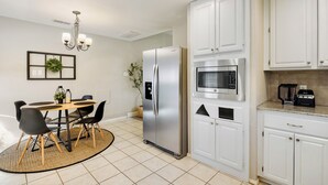 A modern kitchen with white cabinets, a stainless steel refrigerator, a built-in microwave, and a dining area with a round table and chairs. - FIFA2026, Pool + FREE Heated Spa, ATTstadium, Six Flag (Grand Prairie)