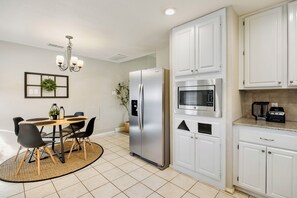 A modern kitchen with white cabinets, a stainless steel refrigerator, a built-in microwave, and a dining area with a round table and chairs. - FIFA2026, Pool + FREE Heated Spa, ATTstadium, Six Flag (Grand Prairie)