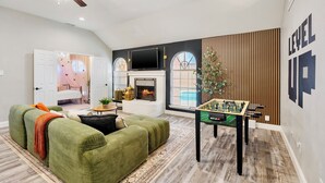 A spacious living room with a green sofa, a foosball table, and a fireplace. - FIFA2026, Pool + FREE Heated Spa, ATTstadium, Six Flag (Grand Prairie)