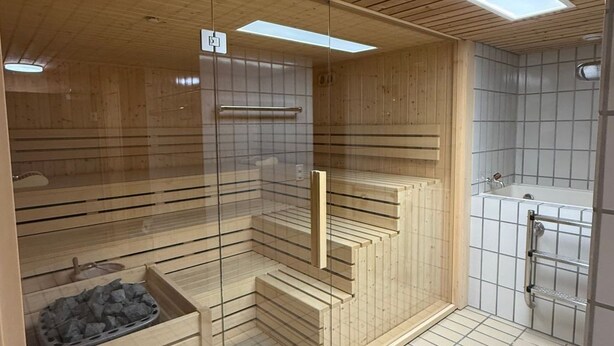 A sauna with wooden slats, a glass door, and a tiled floor. - Studio im Zentrum, Schwimmbad und 400m von Skiliften entfernt by Interhome (St. Moritz)