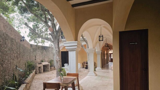 A corridor with arches, a wooden table, and chairs, leading to a door labeled "BANOS". - Casa Lucia B&B Valladolid  (Valladolid)