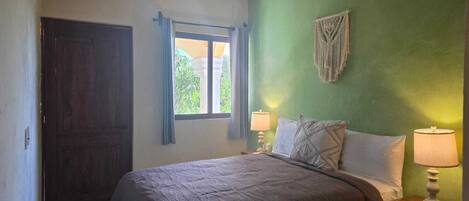 Un dormitorio con cama, dos lámparas de noche, una ventana con cortinas, un ventilador de techo y un equipo de aire acondicionado.