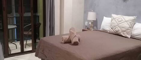 Une chambre avec un lit, une table de chevet, une décoration murale en macramé et une porte-fenêtre coulissante donnant sur un espace extérieur.