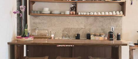 A kitchen with wooden bar stools, a coffee machine, and various kitchenware on shelves.