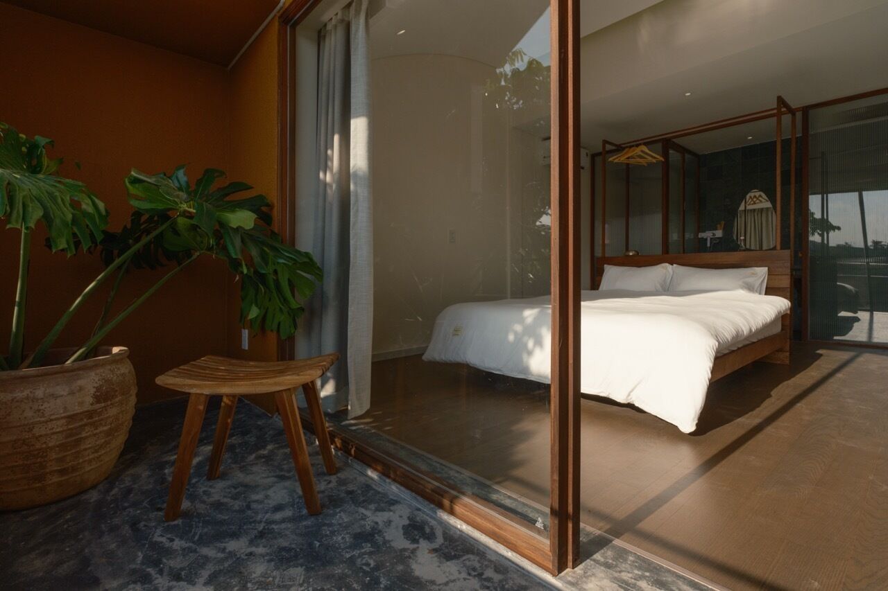 A bedroom with a large bed, a glass door leading to a balcony, and a potted plant.