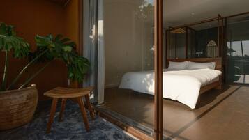 A bedroom with a large bed, a glass door leading to a balcony, and a potted plant.