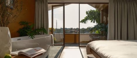 A hotel room with a bed, a sofa, a bathtub, and a large window offering a city view.