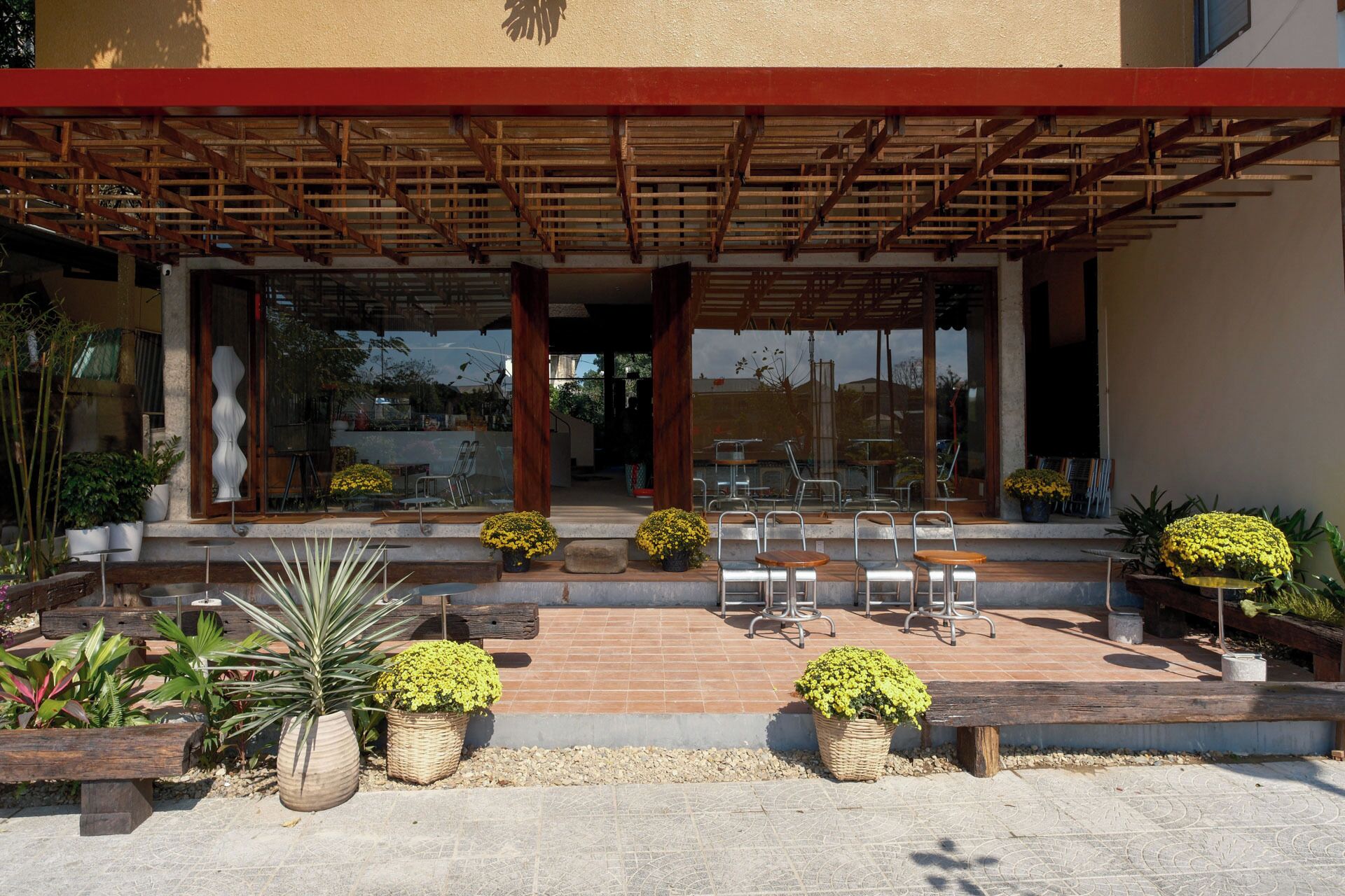 Un área de estar al aire libre con mesas y sillas, rodeada de plantas en macetas y una pérgola de madera.
