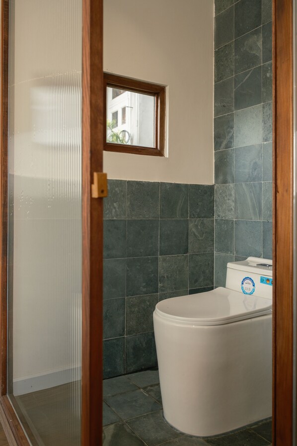 Un baño con una bañera blanca, azulejos verde oscuro y una pequeña ventana sobre el inodoro.