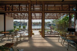 An open-plan cafe with a view of a waterfront, featuring wooden tables and chairs, and a mix of indoor and outdoor seating areas. - Amea Homestay (Hue)