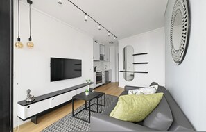 A modern living room with a flat-screen TV, a sofa, a coffee table, and a kitchen in the background. - The Flamingo Sea Point Prom One Bed Balcony (Cape Town)