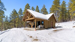 Una cabana de fusta amb un teulat cobert de neu, envoltada d'arbres.