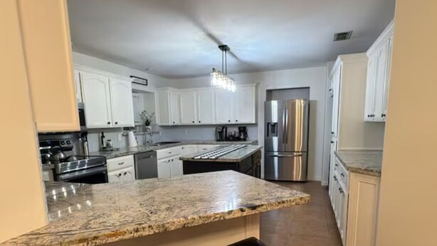 A kitchen with white cabinets, a stainless steel refrigerator, a granite countertop, and two wooden stools. - Spacious 5-bedroom  3.5 bath home on 1/2 an acre in Mission.  Pet friendly. (Mission)