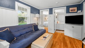 A modern living room with a blue sofa, a flat-screen TV, and a wooden floor. - Charming Cape Cod Cottage with Pool Near Red River Beach (Harwich Port)