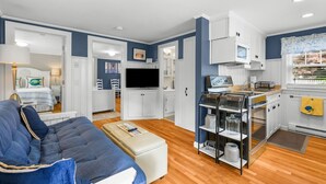 A compact living space with a sofa, a television, a kitchenette, and a dining area. - Charming Cape Cod Cottage with Pool Near Red River Beach (Harwich Port)