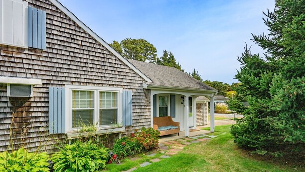 A single-story house with a covered porch, a small garden with stepping stones, and a well-maintained lawn. - Charming Cape Cod Cottage with Pool Near Red River Beach (Harwich Port)