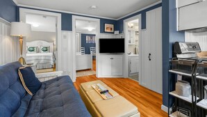 A compact living space with a sofa, a television, a kitchenette, and a bathroom visible through an open door. - Charming Cape Cod Cottage with Pool Near Red River Beach (Harwich Port)