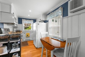 Une cuisine de taille réduite avec des meubles blancs, une table à manger en bois et une fenêtre équipée de stores.