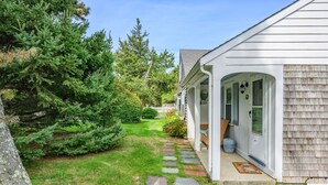 A house with a covered porch, stone pathway, and a well-maintained lawn. - Charming Cape Cod Cottage with Pool Near Red River Beach (Harwich Port)