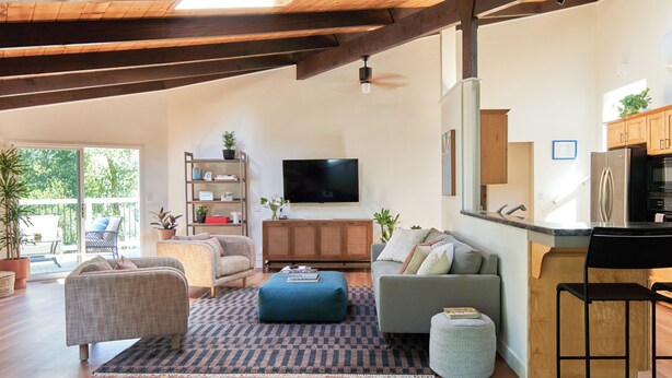 A spacious living area with a sofa, ottoman, and a television. A kitchen area with a refrigerator and cabinets is visible. - Aptos Hills Getaway - Welcome to Oak Landing (Aptos)