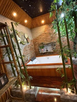 A spa area with a wooden bathtub, bamboo plants, and a stone wall. - Athena Hotel (Thuy Xuan)