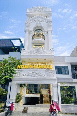 A hotel entrance with a white facade, a central archway, and a sign reading 'ATHENA HOTEL'. - Athena Hotel (Thuy Xuan)