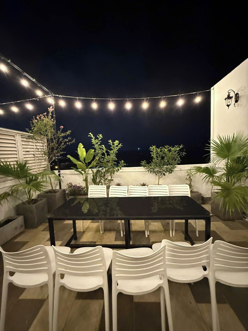 An outdoor patio with a table and chairs, string lights, and potted plants.