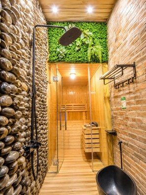 Un sauna doté d’un plancher en bois, d’un mur en pierre, d’un mur végétal, d’un espace douche et d’un porte-serviettes.
