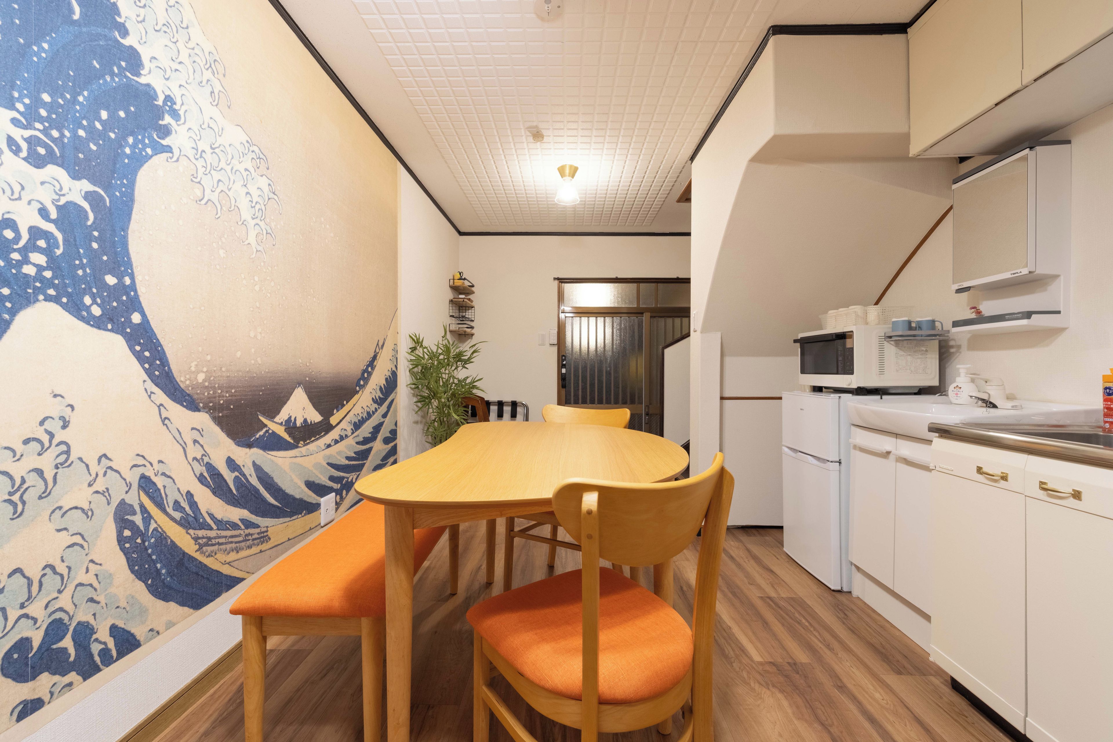 A traditional Japanese-style room with tatami flooring, a low table with cushions, a shoji screen door, and a kitchen area with modern appliances.