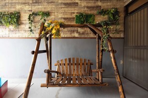 A wooden swing with a bench, set against a brick wall with green foliage decorations. - Authentic Japanese Home: Retro Charm, Modern Comfort, & Play! (大阪市城東区新喜多2丁目3)