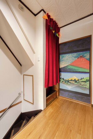 A staircase with a wooden handrail, a red curtain, and a framed artwork of a mountain landscape. - Authentic Japanese Home: Retro Charm, Modern Comfort, & Play! (大阪市城東区新喜多2丁目3)