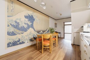 A dining area with a traditional Japanese wave painting on the wall, wooden flooring, and a table with chairs. - Authentic Japanese Home: Retro Charm, Modern Comfort, & Play! (大阪市城東区新喜多2丁目3)
