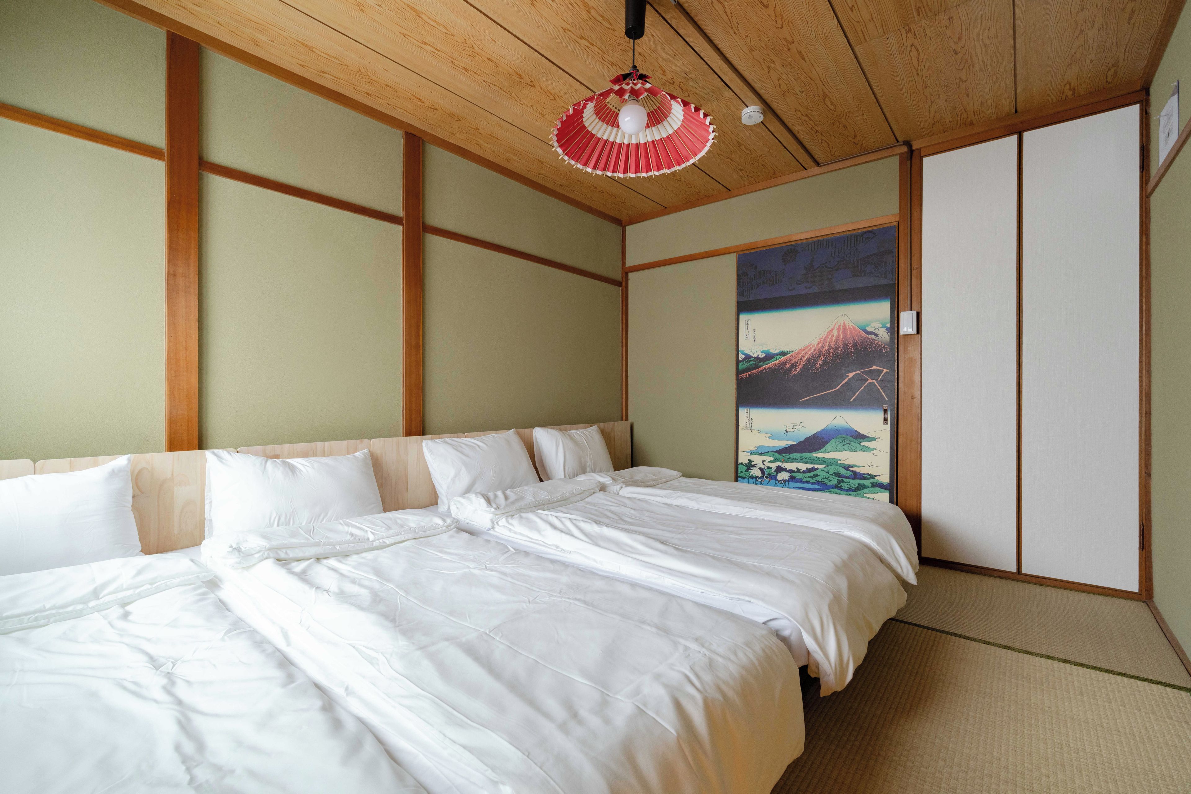 A traditional Japanese-style bedroom with tatami flooring, a low wooden ceiling, and a large bed with white bedding.