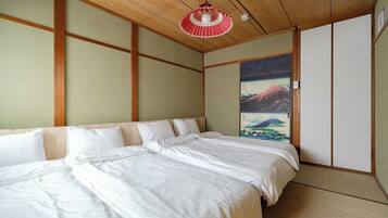 A traditional Japanese-style bedroom with tatami flooring, a low wooden ceiling, and a large bed with white bedding.