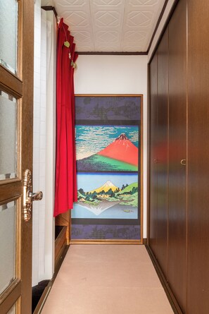 Un couloir avec une porte en bois, un rideau rouge et un grand tableau encadré représentant un paysage de montagne.