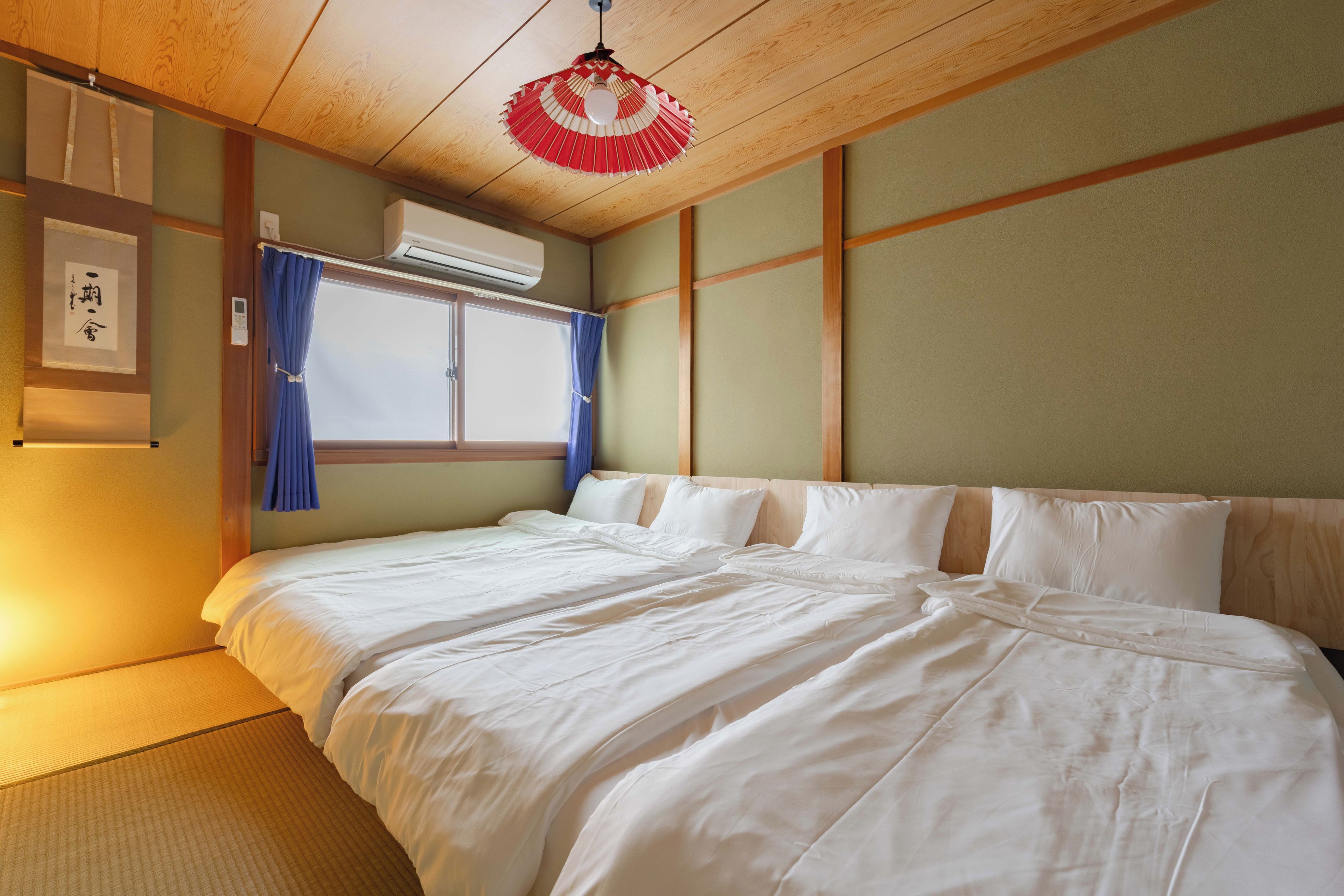 A hotel room with a bed, a window with curtains, an air conditioning unit, and a wall-mounted air conditioner.
