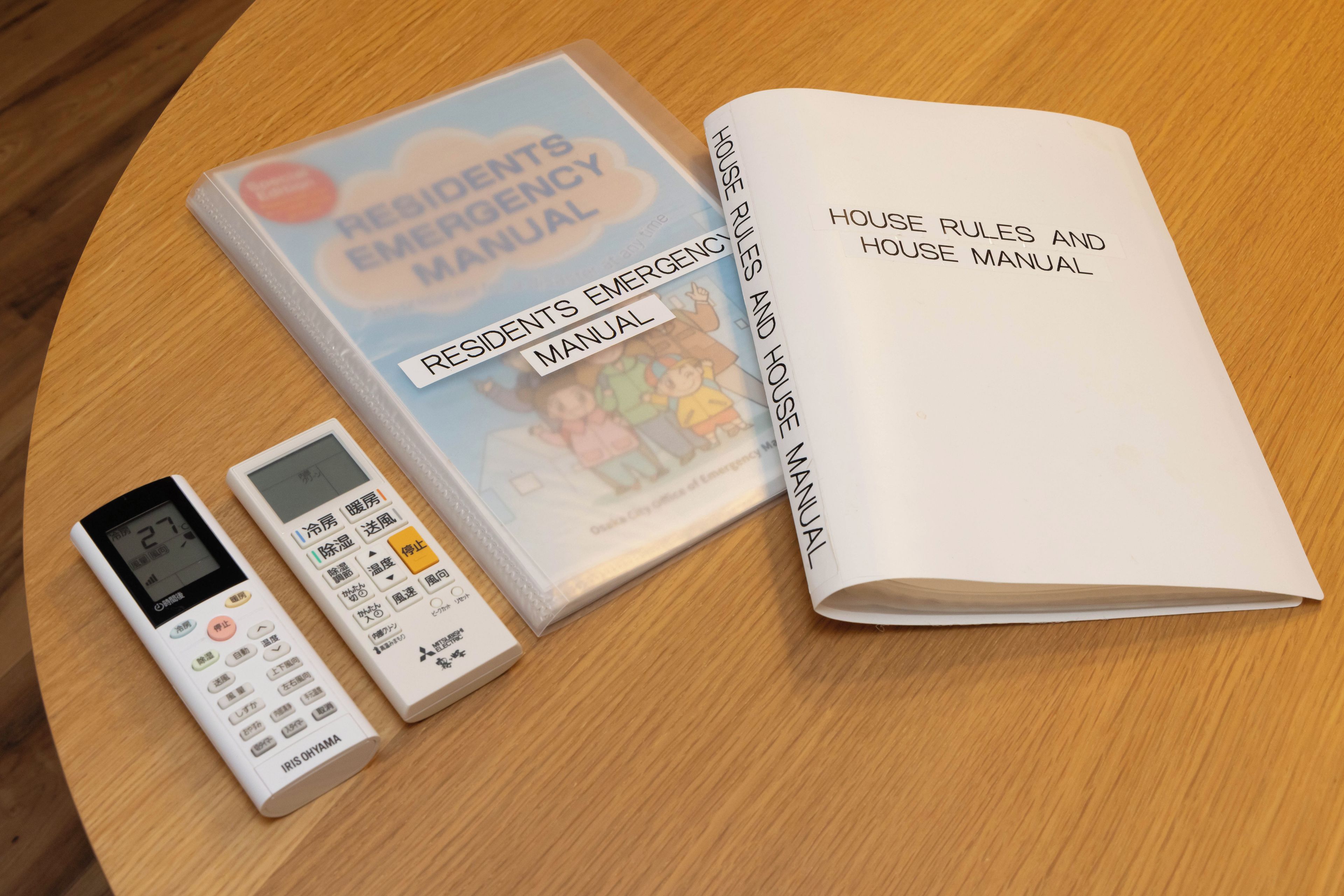 A residents' emergency manual, a house rules and house manual, and a digital thermostat on a wooden surface.