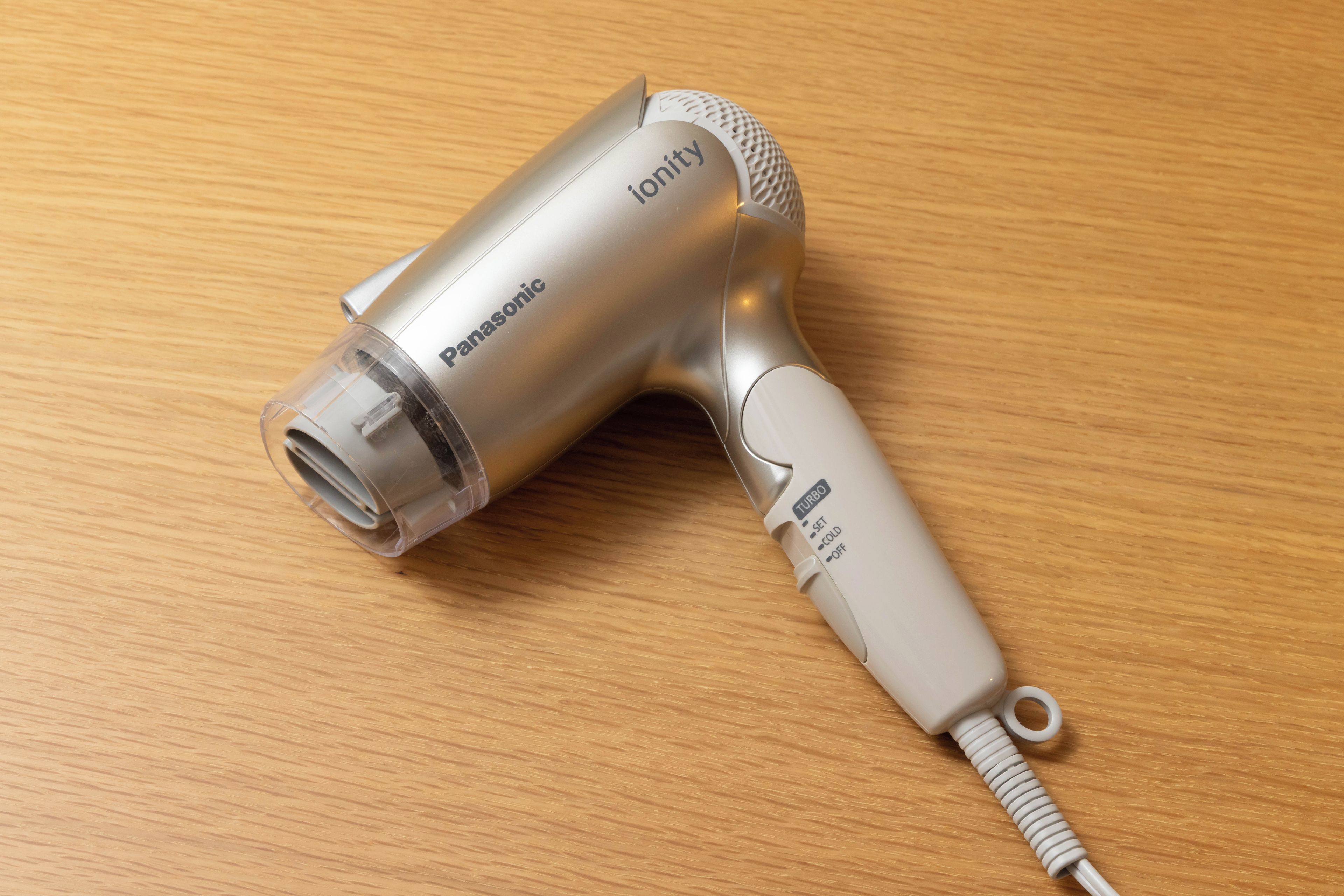 Un sèche-cheveux Panasonic doté d’un embout transparent et d’un panneau de commande placé sur une surface en bois.