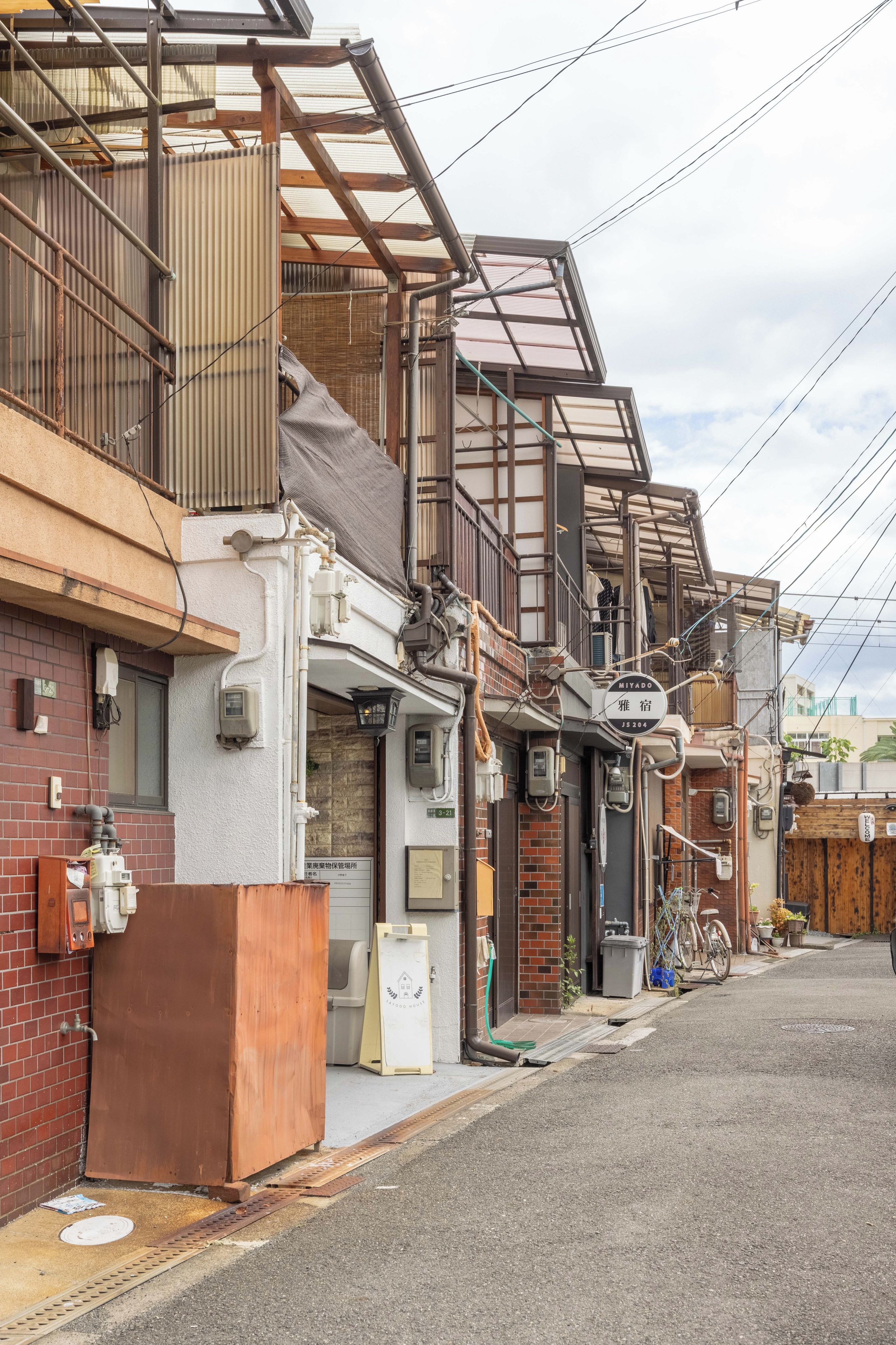 A narrow urban street with traditional Japanese buildings, a bicycle, and a small shop.