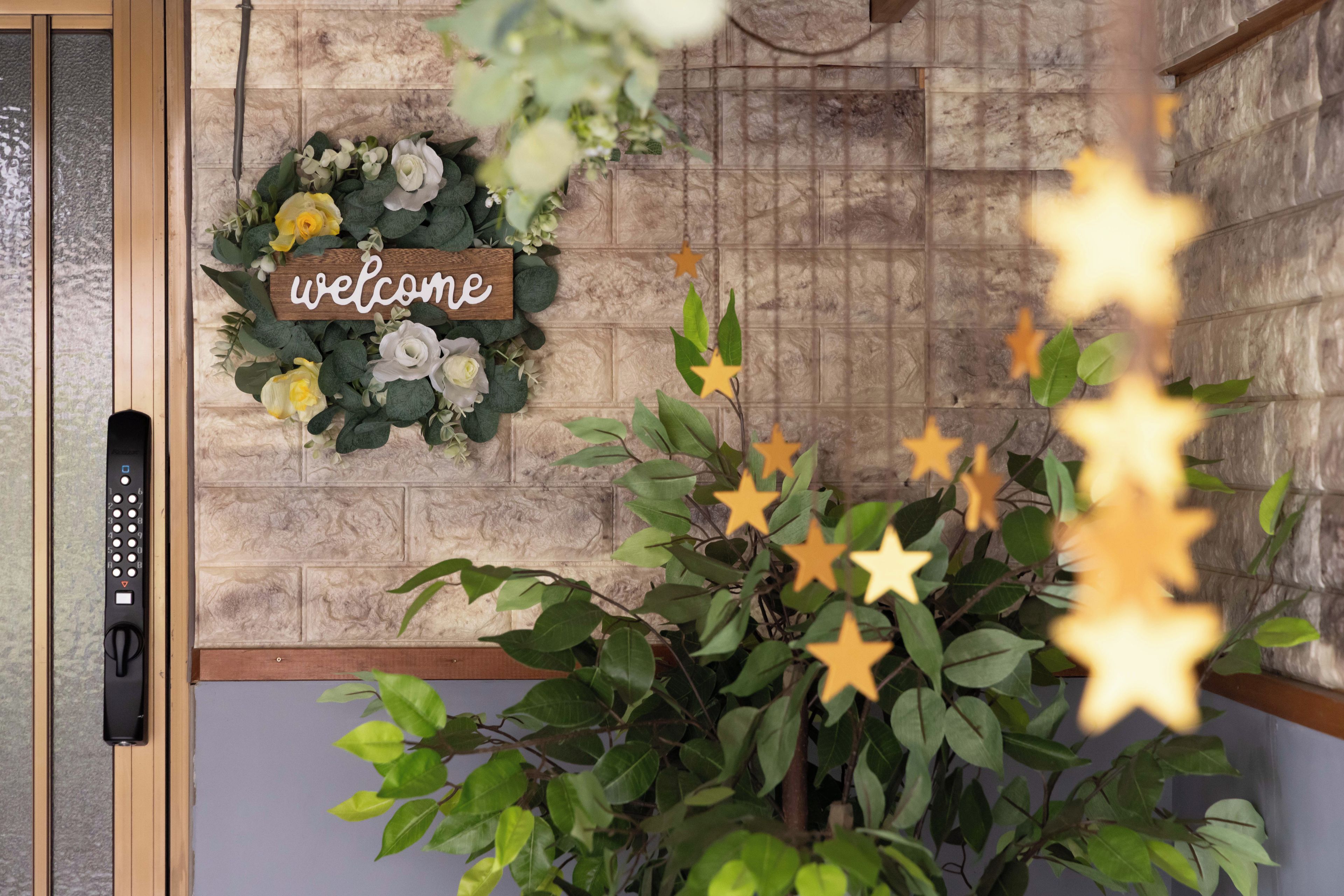 A welcome sign with a floral wreath, a wall with a stone pattern, and a plant with star-shaped decorations.