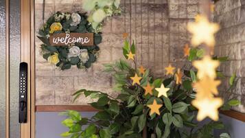 A welcome sign with a floral wreath, a wall with a stone pattern, and a plant with star-shaped decorations.