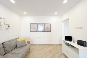 A modern living room with a grey sofa, a white cabinet with a laptop, and three framed artworks on the wall.