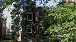 Ein zweistöckiges Haus mit Veranda und kleinem Vorgarten.