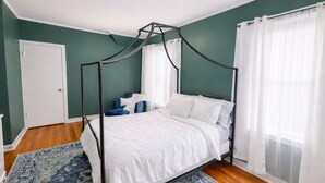 Ein Himmelsbett mit weißer Bettwäsche, ein Teppich in Blau und Weiß sowie eine weiße Tür.