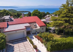 Ein Wohngebäude mit rotem Dach, umgeben von Grün und Blick aufs Meer.