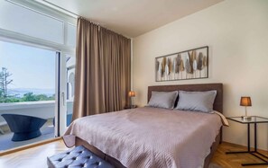 Ein Schlafzimmer mit einem großen Bett, zwei Nachttischlampen, Blick ins Freie und einem Wandbild.