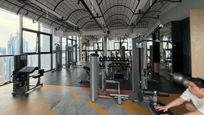 A gym with various exercise equipment, large windows, and a high ceiling. - Metahome@Scarletz Suites KLCC (Kuala Lumpur)