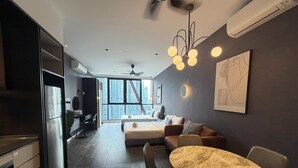A modern kitchen with a refrigerator, dining table, and chairs. There is a sofa and a bed in the living area with a city view. - Metahome@Scarletz Suites KLCC (Kuala Lumpur)