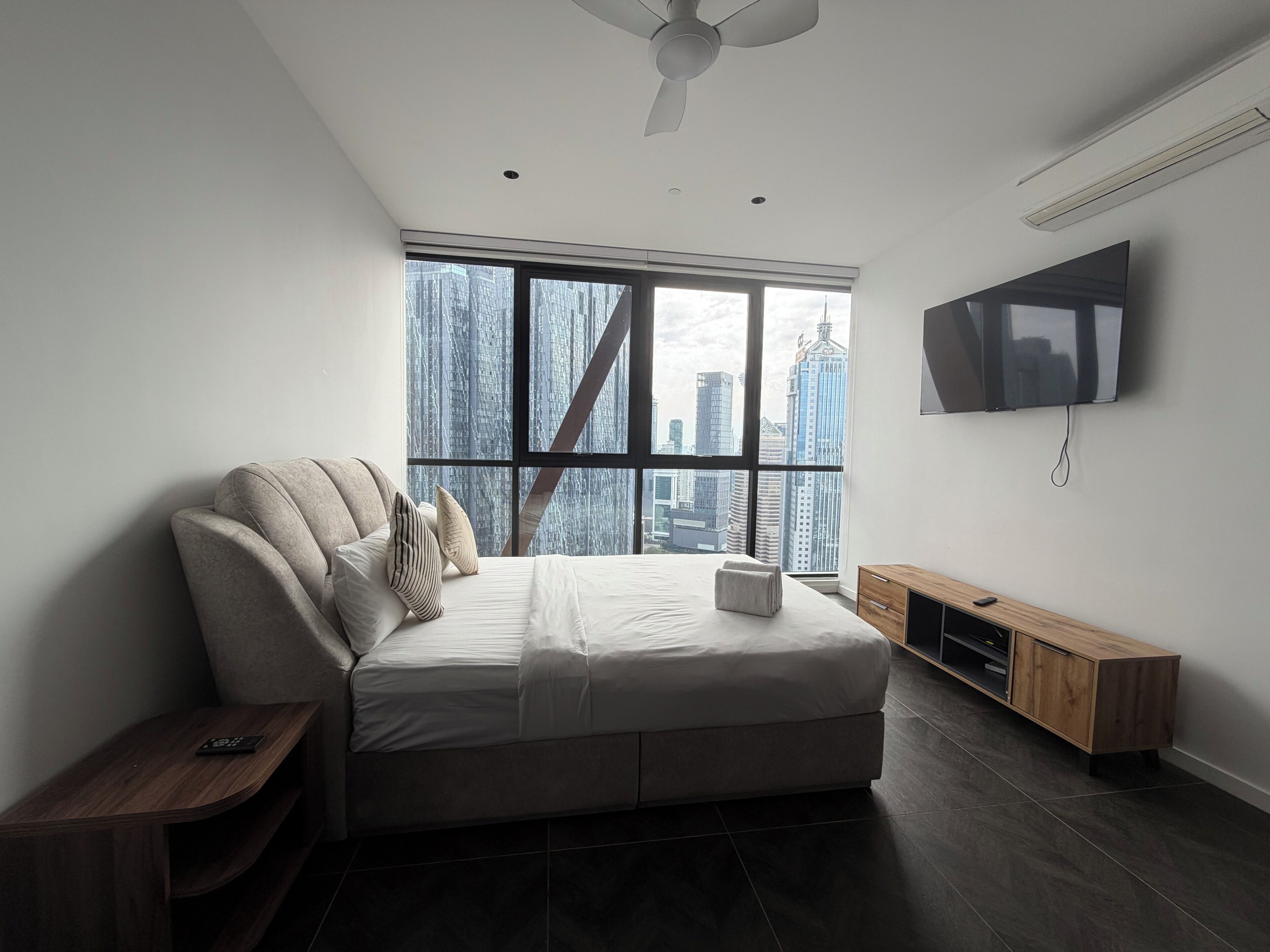 Una camera da letto moderna con un'ampia finestra, un letto, una televisione e un armadio in legno.