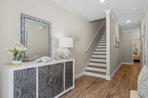 A hallway with a staircase, a console table with decorative items, and a large mirror.